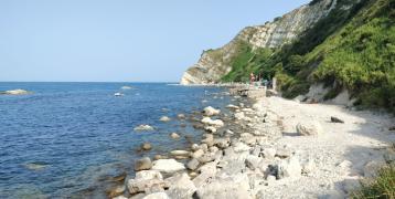 White, rocky seashore and steep slopes rising up from the blue sea.