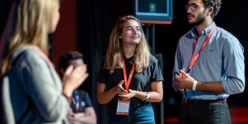  young adults on a stage discussing a project with an audience, during a startup festival