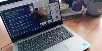 Laptop on a table with an online seminar presentation rolling. In the screen there is a slide with topic of key actions.