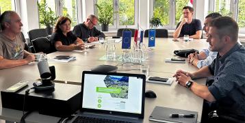 Stakeholders attending the third GIFT Project Regional Stakeholder Group meeting in Zagreb, August 2024. Participants are seated around a conference table, engaged in discussions with a laptop displaying the GIFT project presentation in the foreground. European Union and Croatian flags are on display.