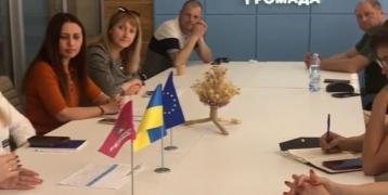People sitting at around a table, and there is writing in Ukranian on the back wall.