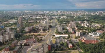 Aerial view of Vilnius, the capital city of Lithuania, showcasing its urban landscape, modern architecture, and green spaces, with vast stretches of forests visible in the background.